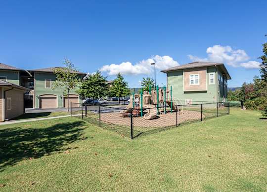 A playground with a green fence and a slide.