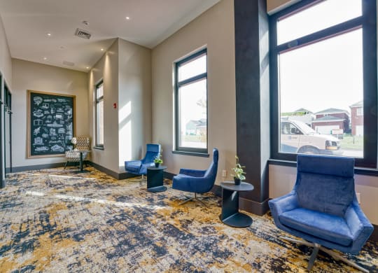 a lobby with blue chairs and a chalkboard on the wall and three large windows