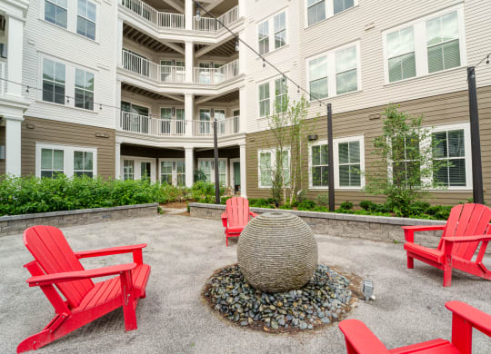 a fire pit with red chairs in front of an apartment building