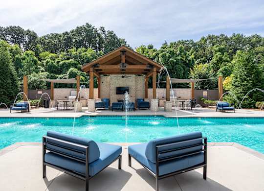 A pool with a wooden pavilion and lounge chairs.