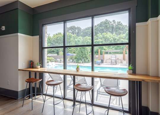 A room with a long table and chairs with a view of a pool and trees outside.