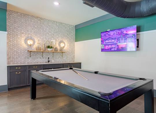 A pool table is in the middle of a room with a TV on the wall.