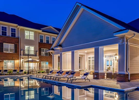 a swimming pool with chaise lounge chairs and an umbrella in front of a building at Canopy at Ginter Park Apartments in Virginia 23227