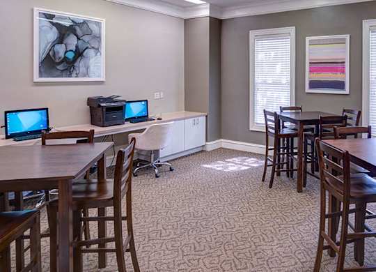 A room with a dining table and chairs, a computer desk with two monitors, and a bookshelf at Austin Chase Apartments, Macon, Georgia
