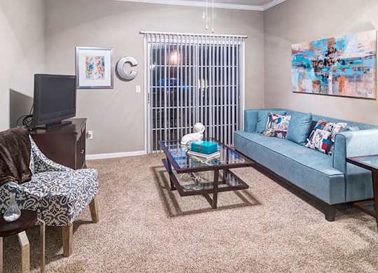 A living room with a blue couch, a chair with a blanket, a coffee table, and a television at Austin Chase Apartments, Macon, 31210