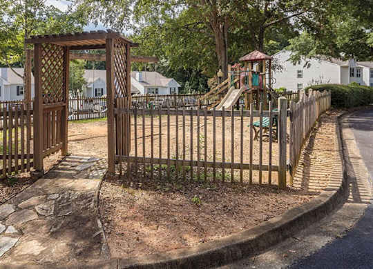 A playground with a wooden gate and a slide is surrounded by a fence.