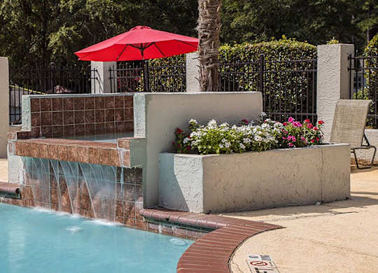 A pool with a red umbrella and a waterfall.