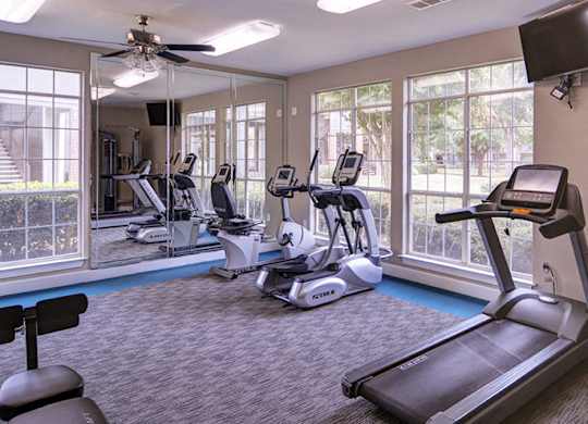A spacious gym with treadmills, elliptical machines, and a television at Huntington Chase Apartments, Warner Robins, Georgia