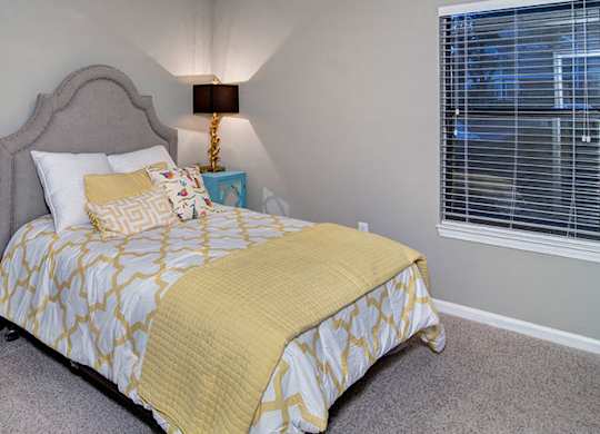 A bed with a yellow comforter and pillows sits in a room with a grey headboard.
