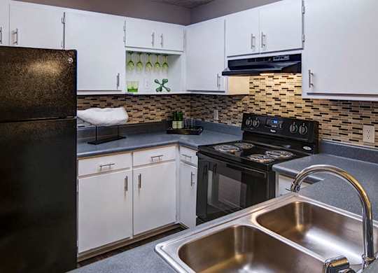 A black refrigerator stands next to a sink in a kitchen.
