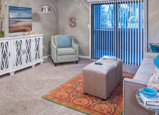 A room with a white cabinet, a grey armchair, and a wooden ottoman.