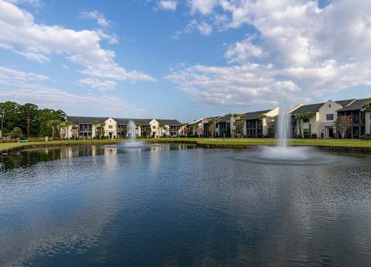 A fountain in the middle of a lake in front of apartment buildings.