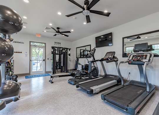 A spacious gym with treadmills, elliptical machines, and a ceiling fan.