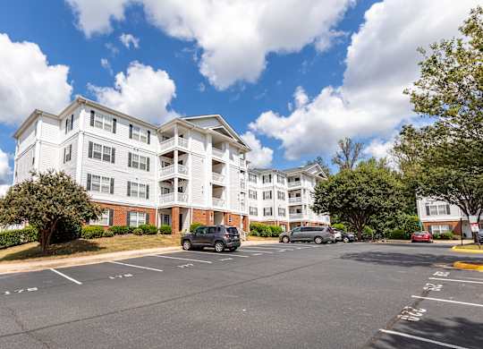 A large white apartment building with a parking lot in front.