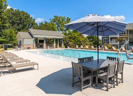 A poolside table and chairs are set up under an umbrella.