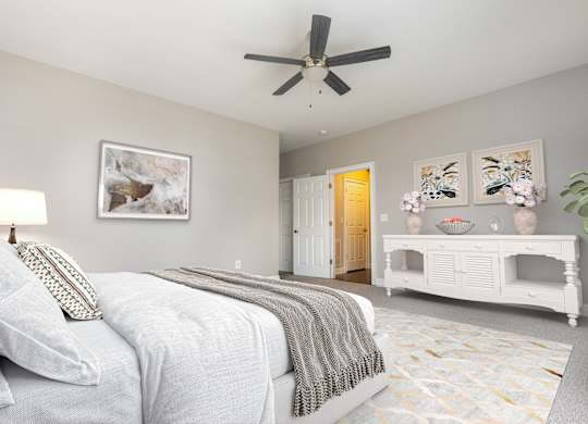 A bedroom with a bed, a fan, and a painting on the wall.