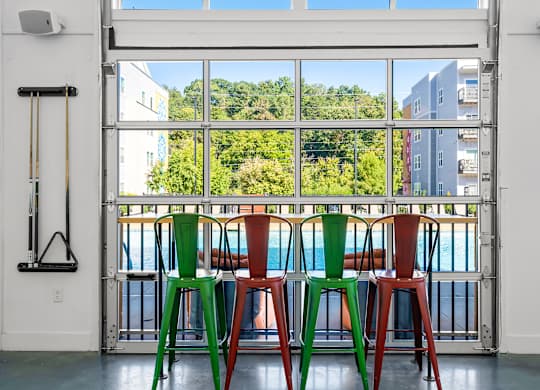 Four colorful stools are lined up in front of a window.