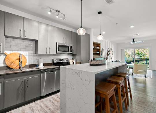 A modern kitchen with a marble island and wooden stools.