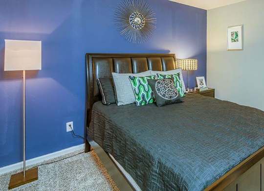 A bedroom with a bed, a lamp, and a mirror. at The Colony at South Park, Aiken, 28903