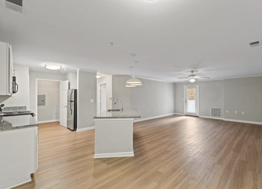 an empty living room and kitchen with wood flooring and white walls at SomerHill Farms Apartments, Gainesville