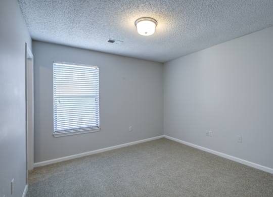 A room with a window covered by white blinds at Southland Station Apartments in Georgia, 31088