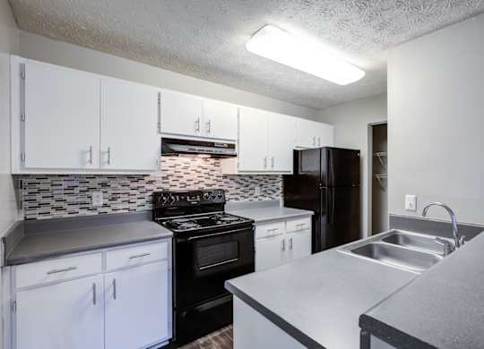 A kitchen with black and white cabinets and a tiled backsplash at Southland Station Apartments in GA, 31088