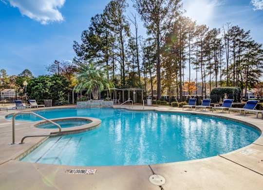 A large outdoor swimming pool surrounded by trees and lounge chairs at Southland Station Apartments in Warner Robins, 31088