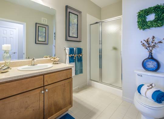 A bathroom with a white toilet, a sink, a mirror, a wreath, and a glass door shower.