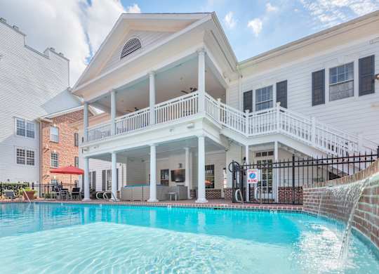 A pool in front of a white house with a balcony.