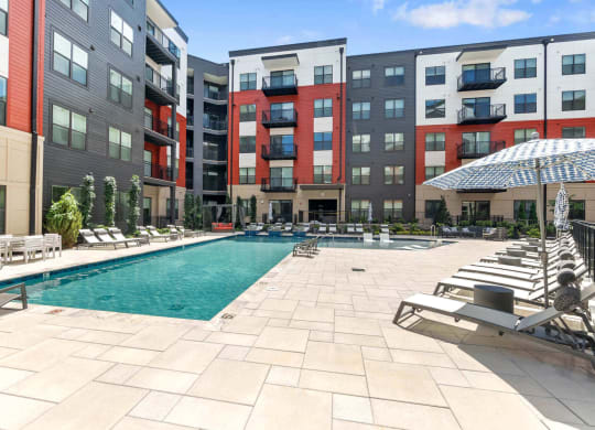 a swimming pool with chaise lounge chairs and umbrellas in front of an apartment building at Tapestry West, Richmond, VA