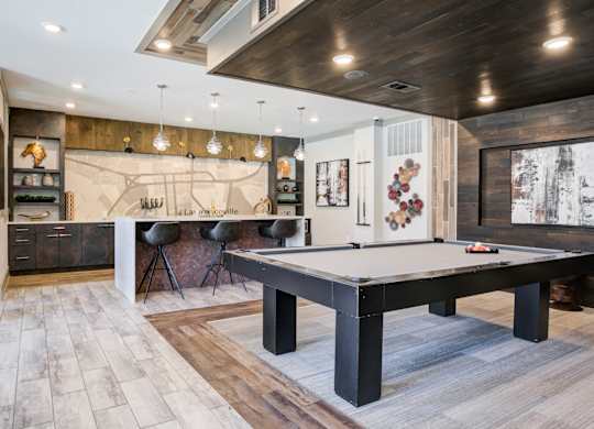 A billiard table is in the middle of a room with wood flooring.