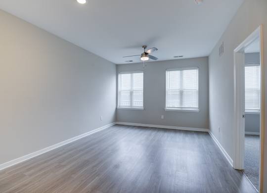 A room with a ceiling fan and two windows.