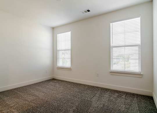 A room with carpeted floor and two windows.