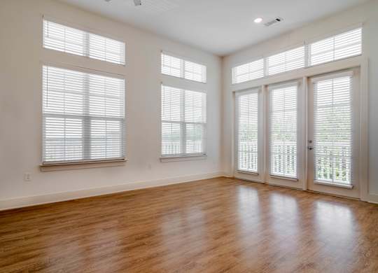 A room with wooden floors and three windows with blinds.