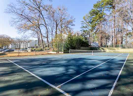 A tennis court surrounded by trees and a fence.