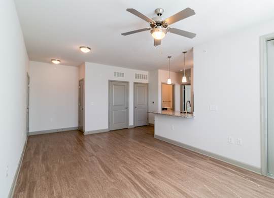 A room with a ceiling fan and light fixture, wooden flooring, and white walls.