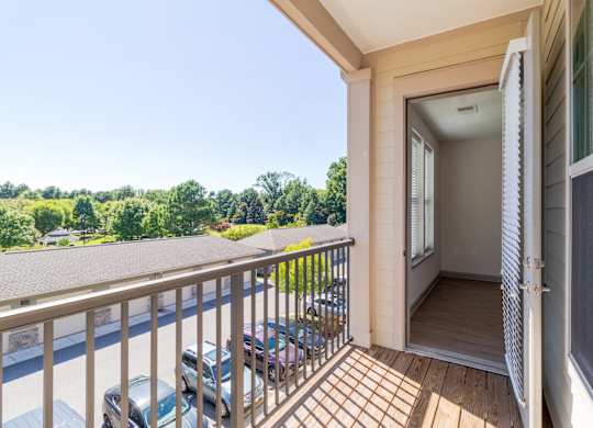 A balcony with a railing and a view of a parking lot and trees.