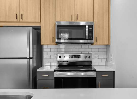 A kitchen with a stainless steel refrigerator, a microwave above the stove, and wooden cabinets.