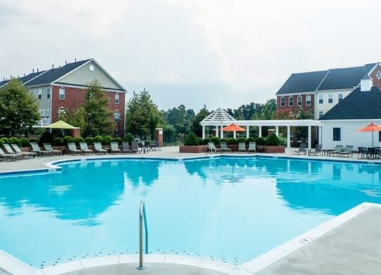a large blue pool with lounge chairs and umbrellas in front of a building at Flats at West Broad Village, Glen Allen Virginia