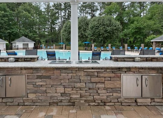 an outdoor kitchen with a pool in the background at Trails at Short Pump Apartments, Virginia,23233
