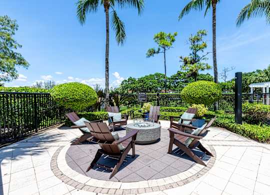 A patio with a fire pit and chairs surrounded by a black fence.