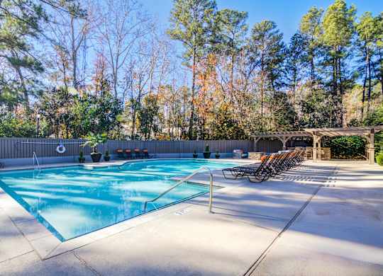 A pool surrounded by trees and a fence with chairs around it.