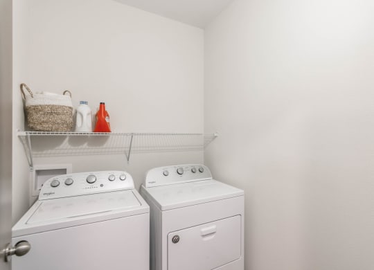 a washer and dryer in a white laundry room with a shelf above them at Village at Westland Cove Apartments, Knoxville, TN