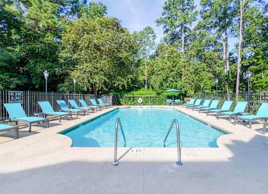 A large swimming pool surrounded by trees and lounge chairs.