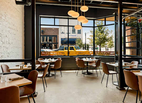 A restaurant with tables and chairs and a view of the street outside.
