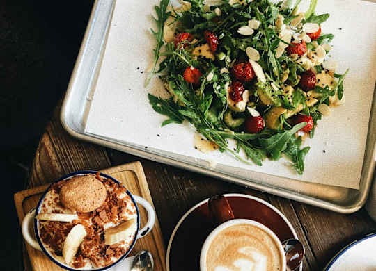 A tray with a salad, a dessert, and a cup of coffee on a wooden table.