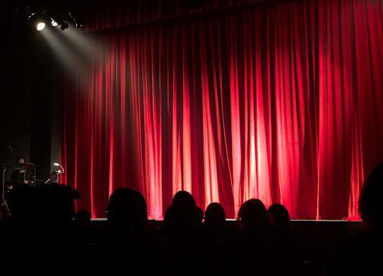 A red curtain on a stage with people watching.