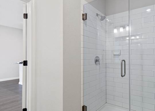 A white tiled shower with a glass door and a silver handle.