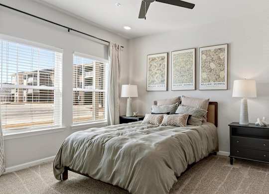 A bedroom with a large bed, a ceiling fan, and a view of a street outside the window.