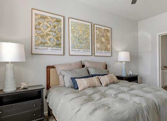 A bedroom with a bed, two lamps, and three framed pictures on the wall.